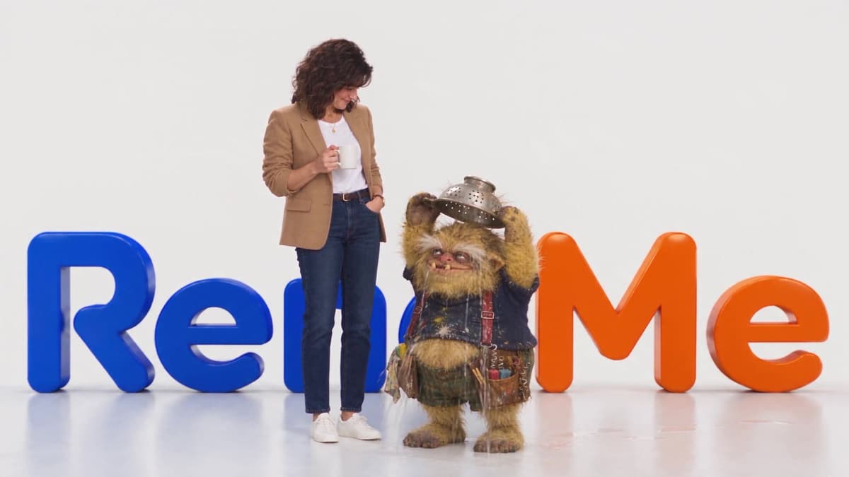 The homeowner from our ads in a bright studio, next to a goblin wearing a colander, behind the RenoMe logo.